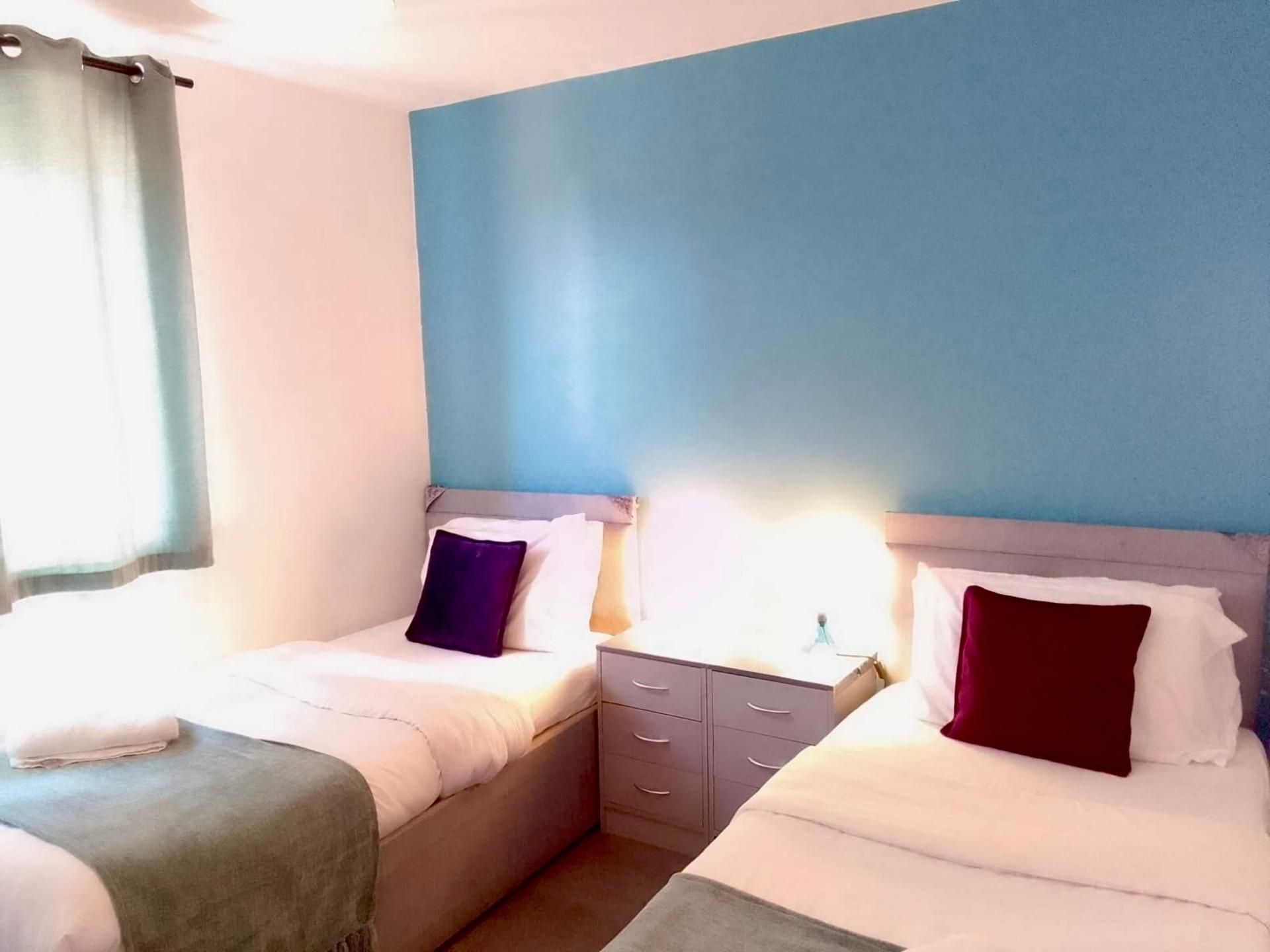 A hotel room with two beds, a nightstand, and a window with curtains.