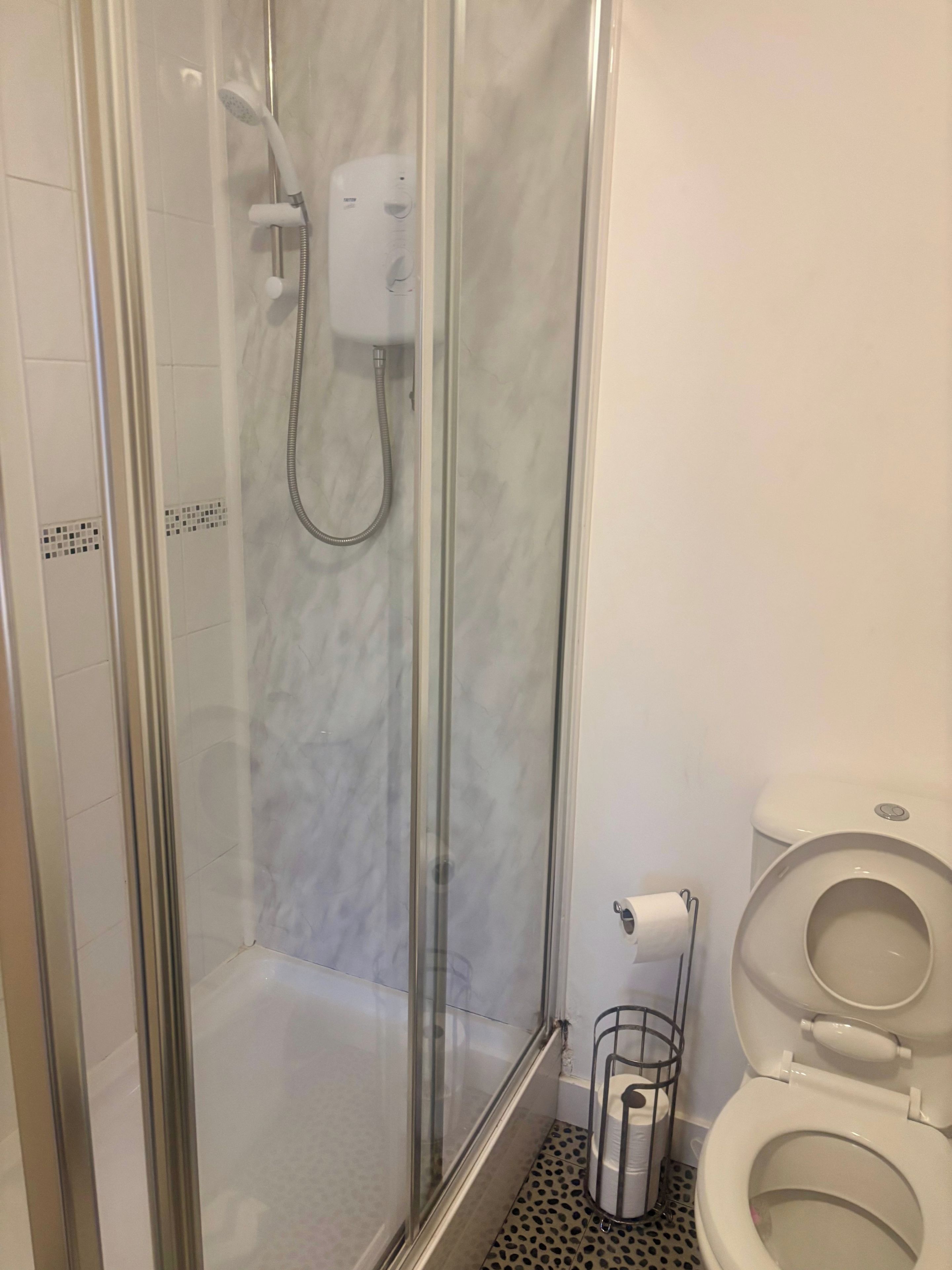 Ein Duschbereich mit Glasabtrennung, einer Handbrause und einem fest installierten Bedienfeld.
