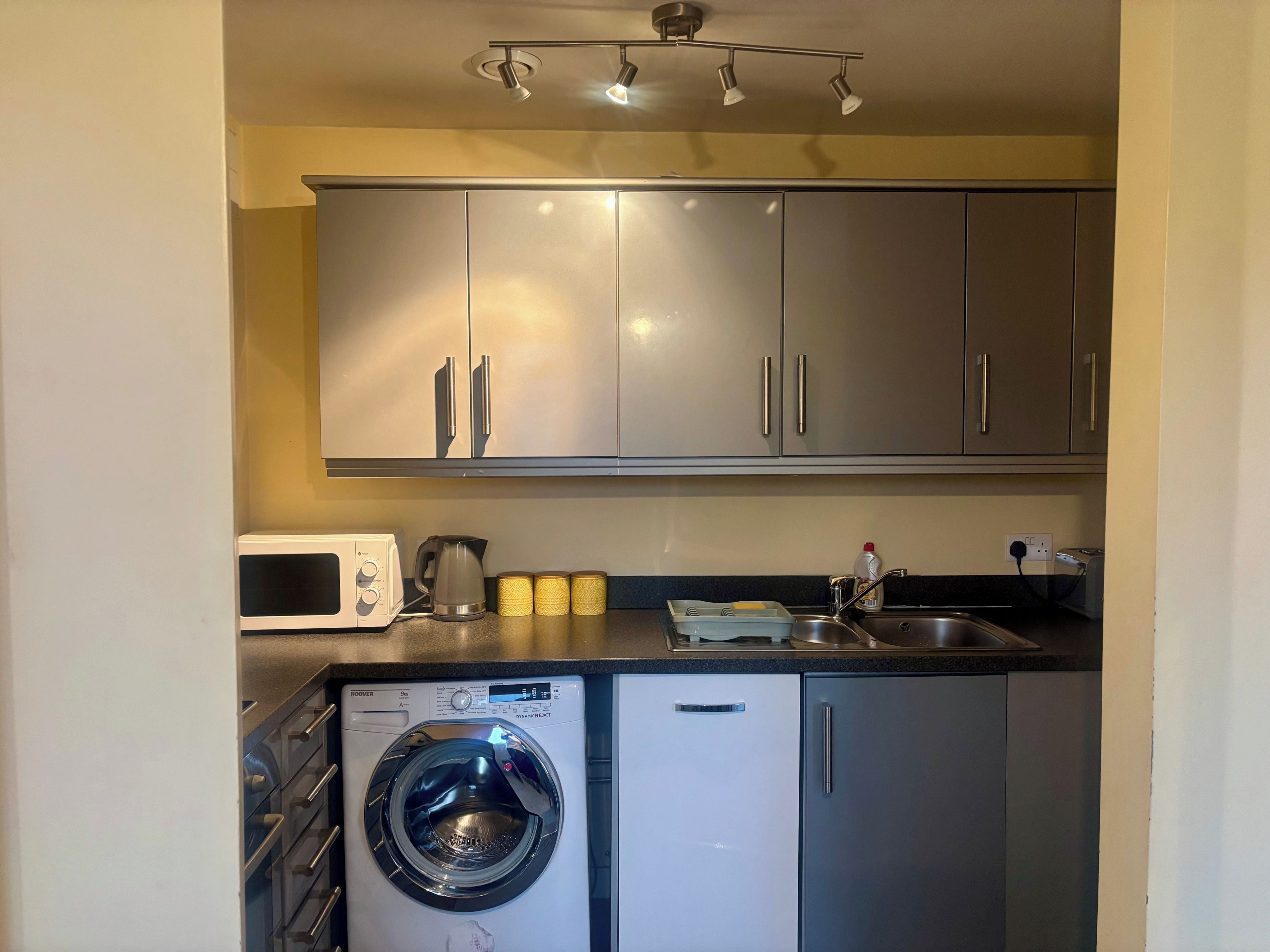 Una cocina compacta con lavadora integrada, microondas y fregadero.