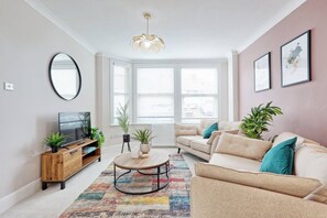 A living room with a sofa, coffee table, TV, and plants.