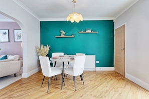 Un espace repas avec une table et des chaises blanches, des murs de couleur turquoise et un plancher en bois.