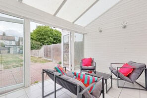 Une terrasse ensoleillée avec une porte vitrée donnant sur un jardin, aménagée avec deux chaises et une table.