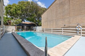 A swimming pool with a covered area, a lifebuoy, and a brick wall in the background. - 3BR Sea Castles condo near Amelia Island beach with pool (Fernandina Beach)