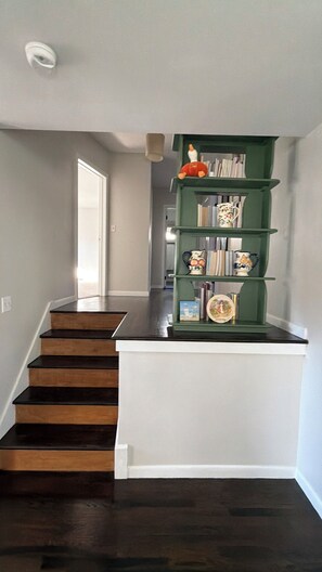 A staircase with dark wooden steps leading to a landing. A green bookshelf with decorative items is placed on the landing.