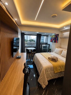 A hotel room with a bed, a desk, a chair, a television, a balcony, and a painting. - Ibirapuera luxurious premium studio with gym and co-working space (São Paulo)