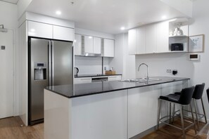 A modern kitchen with a stainless steel refrigerator, a built-in oven, and a large island with a sink. - Sierra Grand Spacious 3 Bedroom Apartment (Broadbeach)