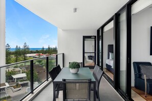 A balcony with a table and chairs, a potted plant, and a view of the sea and buildings. - Sierra Grand Spacious 3 Bedroom Apartment (Broadbeach)