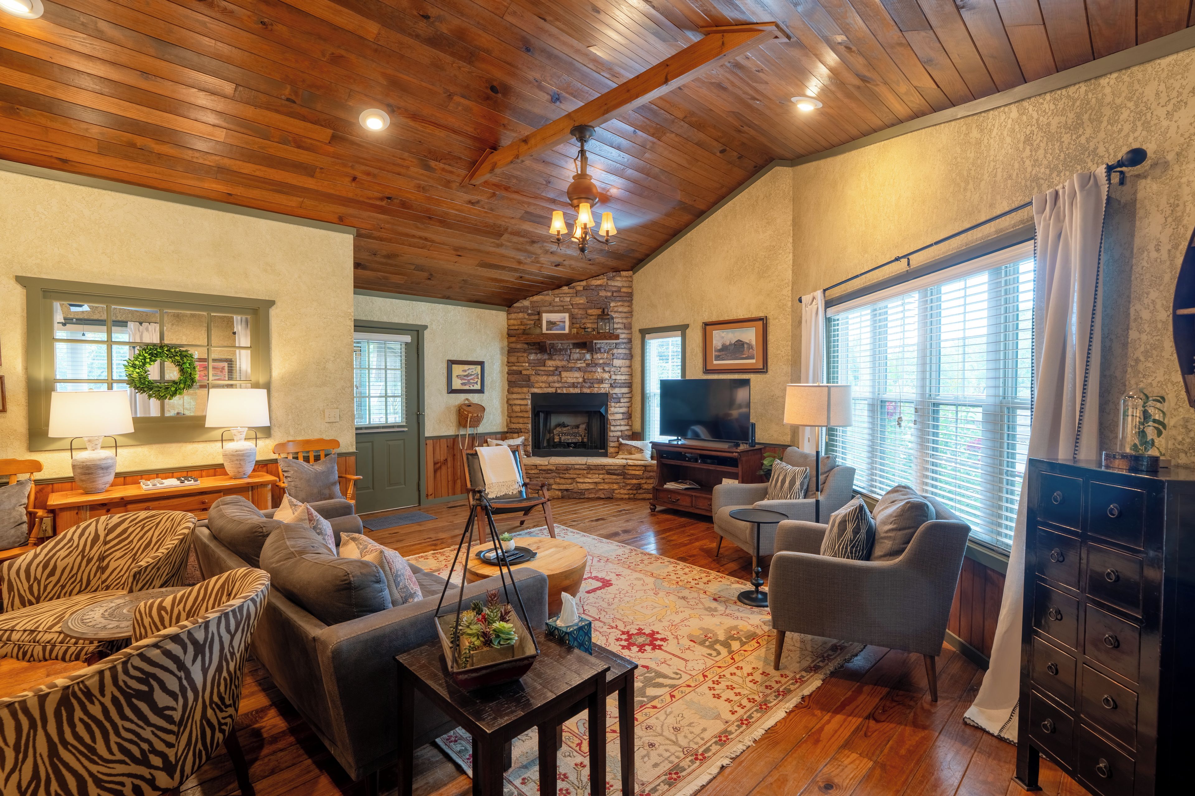 A cozy living room with a fireplace, wooden ceiling, and a stone wall.