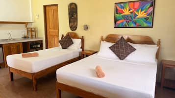 A hotel room with two single beds, a wooden headboard, a colorful abstract painting, a wooden door, and a small table with a cup.