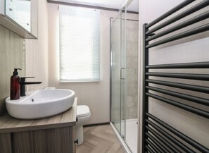 A modern bathroom with a large white sink, a toilet, a glass shower enclosure, and a towel rack. - Cabin Sleeps 6 with Parking (Eyemouth)