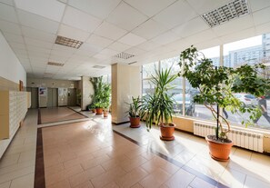 A hallway with tiled flooring, potted plants, a radiator, and a view of the street through large windows. - Grzybowska Skyline Studio (Wola)