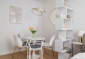 A modern dining area with a white table, chairs, and a vase of yellow flowers. - Park Mirowski Signature Apartment (Warszawa)