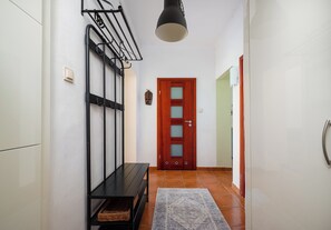 A hallway with a black bench, a wall-mounted rack, a wooden door with glass panels, and a patterned rug on the floor. - Metro Racławicka Cosy Apartment (Warszawa)
