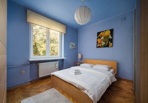A bedroom with a bed, a window, a radiator, a painting, and a lamp. - Metro Racławicka Cosy Apartment (Warszawa)