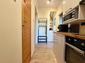 A narrow kitchen with a wooden door, a black drying rack, a microwave, and a clock displaying 23:30. - Dworcowa Old Town Studio (Wrocław)