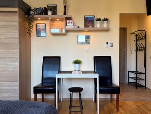Une pièce avec un plancher en bois, deux chaises noires, une table blanche et une petite plante en pot.