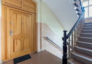 Eine Holztür mit einem Metallgriff, einer schwarzen Handläufe und einer Teppichstufen-Treppe.