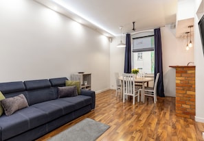 A modern living room with a dark sofa, a dining table with chairs, and a brick accent wall. - Małkowskiego Downtown Apartment (Szczecin)
