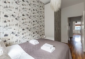 A bedroom with a patterned wallpaper, a bed with a grey quilt, and a white towel. - Małkowskiego Downtown Apartment (Szczecin)