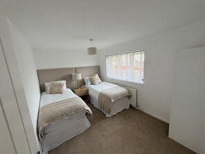 A bedroom with two beds, a window with blinds, a bedside table with a lamp, and a radiator. - House Sleeps 5 with Enclosed Garden (Corby)