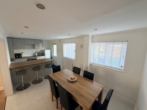 A modern kitchen with a wooden countertop, bar stools, and a dining table with chairs. - House Sleeps 5 with Enclosed Garden (Corby)