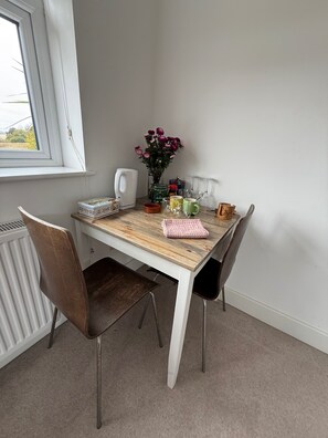 A dining table with chairs, a vase with flowers, a kettle, and various kitchen items.