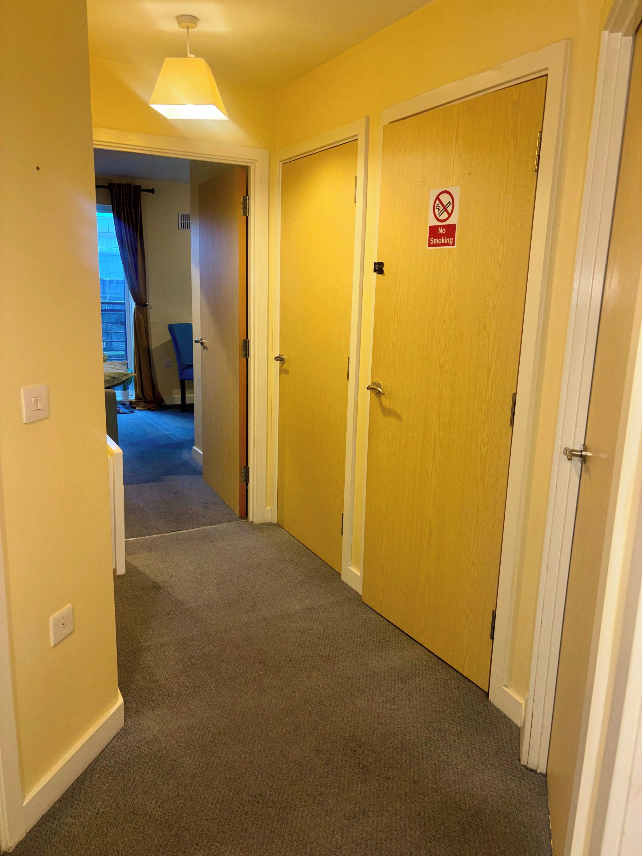 A hallway with carpeted floors and wooden doors, one of which has a 'No Smoking' sign.
