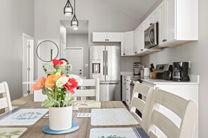 A modern kitchen with white cabinetry, stainless steel appliances, and a dining area with a wooden table and chairs. - Downtown Retreat Wi-Fi Unrestricted Parking (Indianapolis)