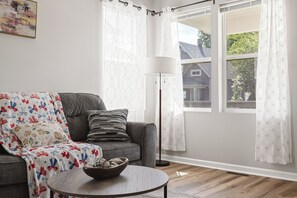A living room with a grey sofa, a patterned throw blanket, a small round table with a bowl, and a floor lamp. - Downtown Retreat Wi-Fi Unrestricted Parking (Indianapolis)
