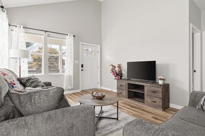 A living room with a sofa, a coffee table, a TV on a wooden stand, and a door with a window. - Downtown Retreat Wi-Fi Unrestricted Parking (Indianapolis)