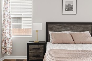 A bedroom with a bed, a nightstand, a lamp, a window with blinds, and a framed picture on the wall. - Downtown Retreat Wi-Fi Unrestricted Parking (Indianapolis)