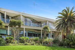 A modern multi-story building with balconies, surrounded by lush greenery and palm trees. - Upstairs Resort Apartment (Anglesea)