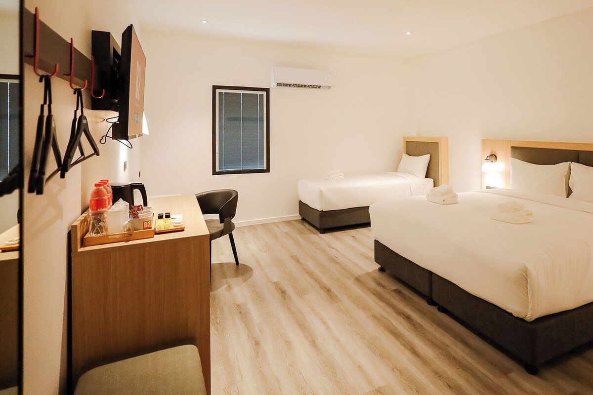 A hotel room with a large bed, a smaller bed, a desk with a chair, and a window.