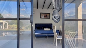 Un dormitorio con una cama azul, un cuadro en la pared y vistas a través de un ventanal.