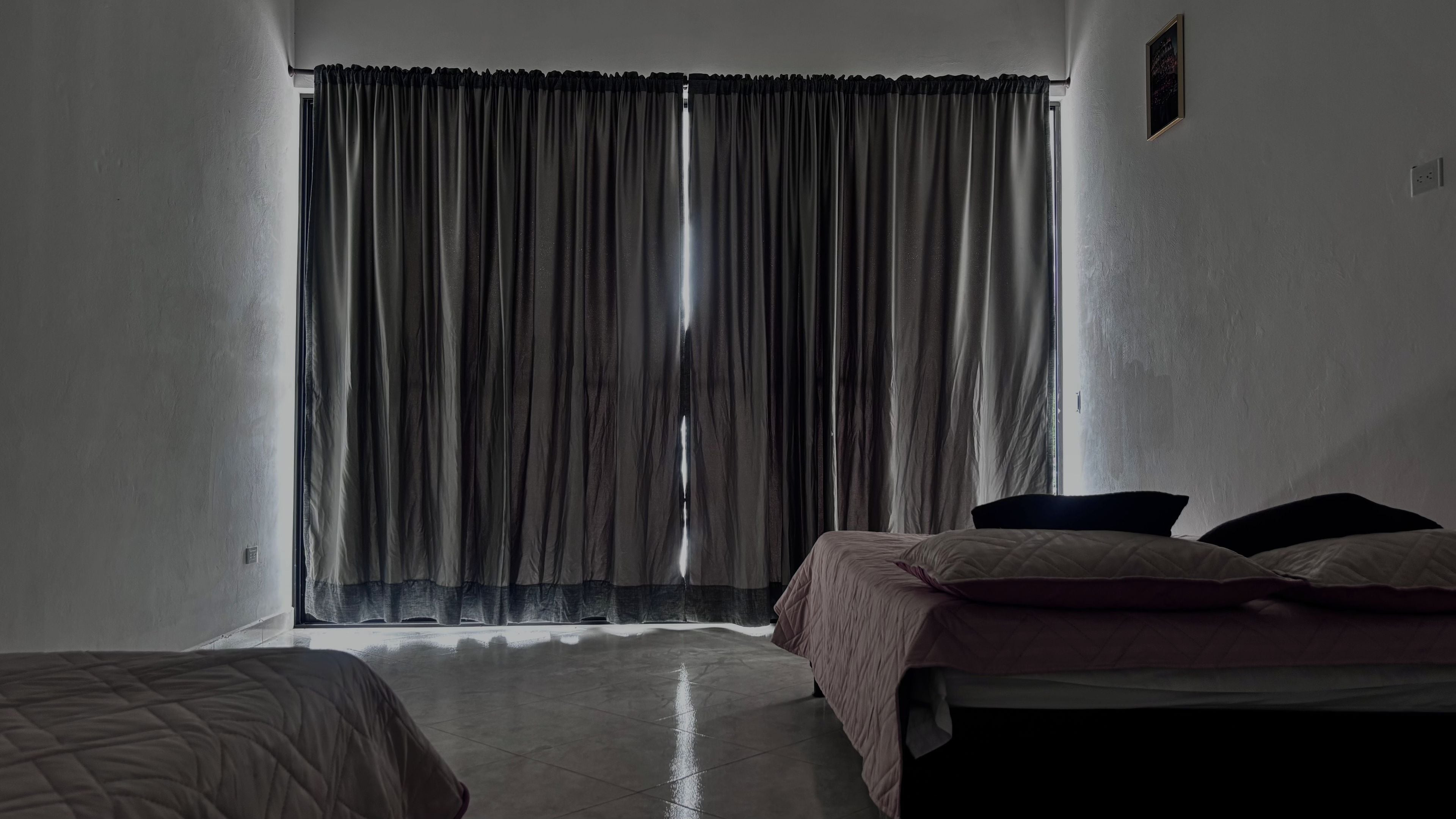 Un dormitorio con cama, ventana con cortinas y un interruptor de luz en la pared.
