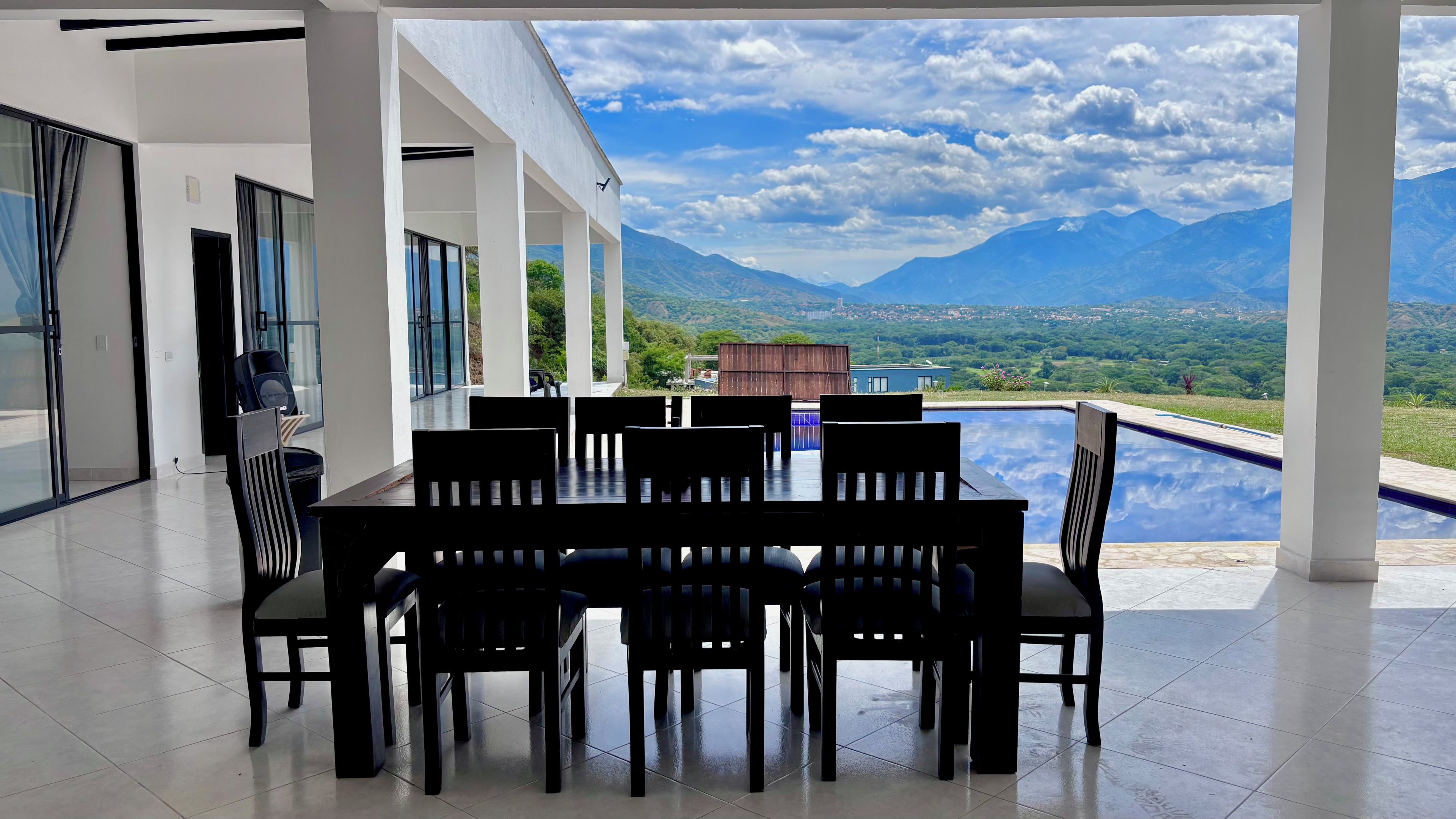 A modern dining area with a pool view, featuring a table and chairs, and a clear sky.