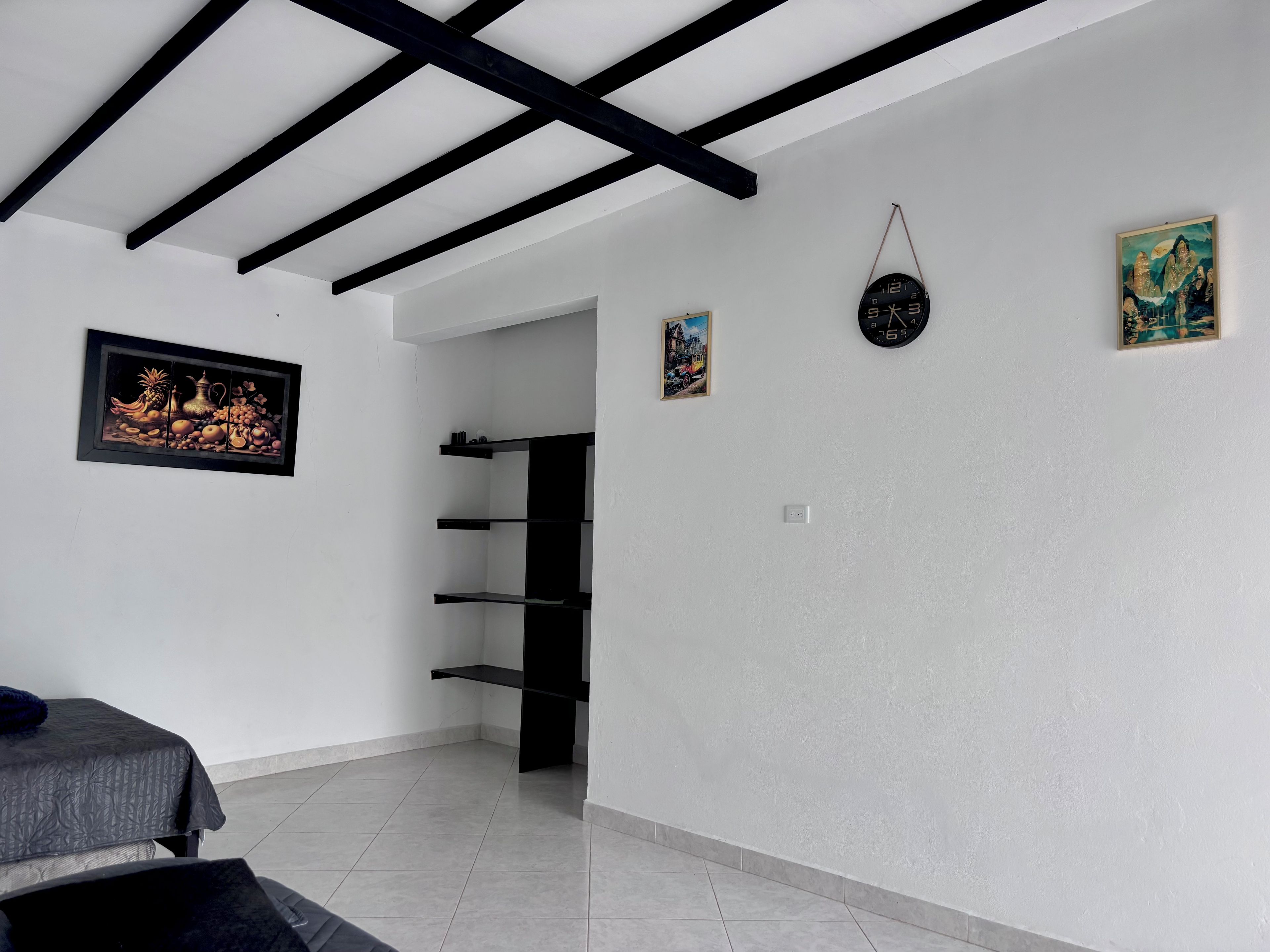 A room with a bed, a black shelf unit, a wall clock, and a framed picture.