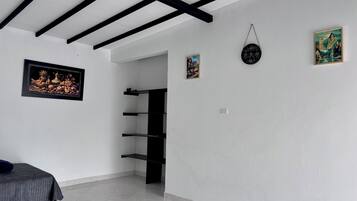 A room with a bed, a black shelf unit, a wall clock, and a framed picture.