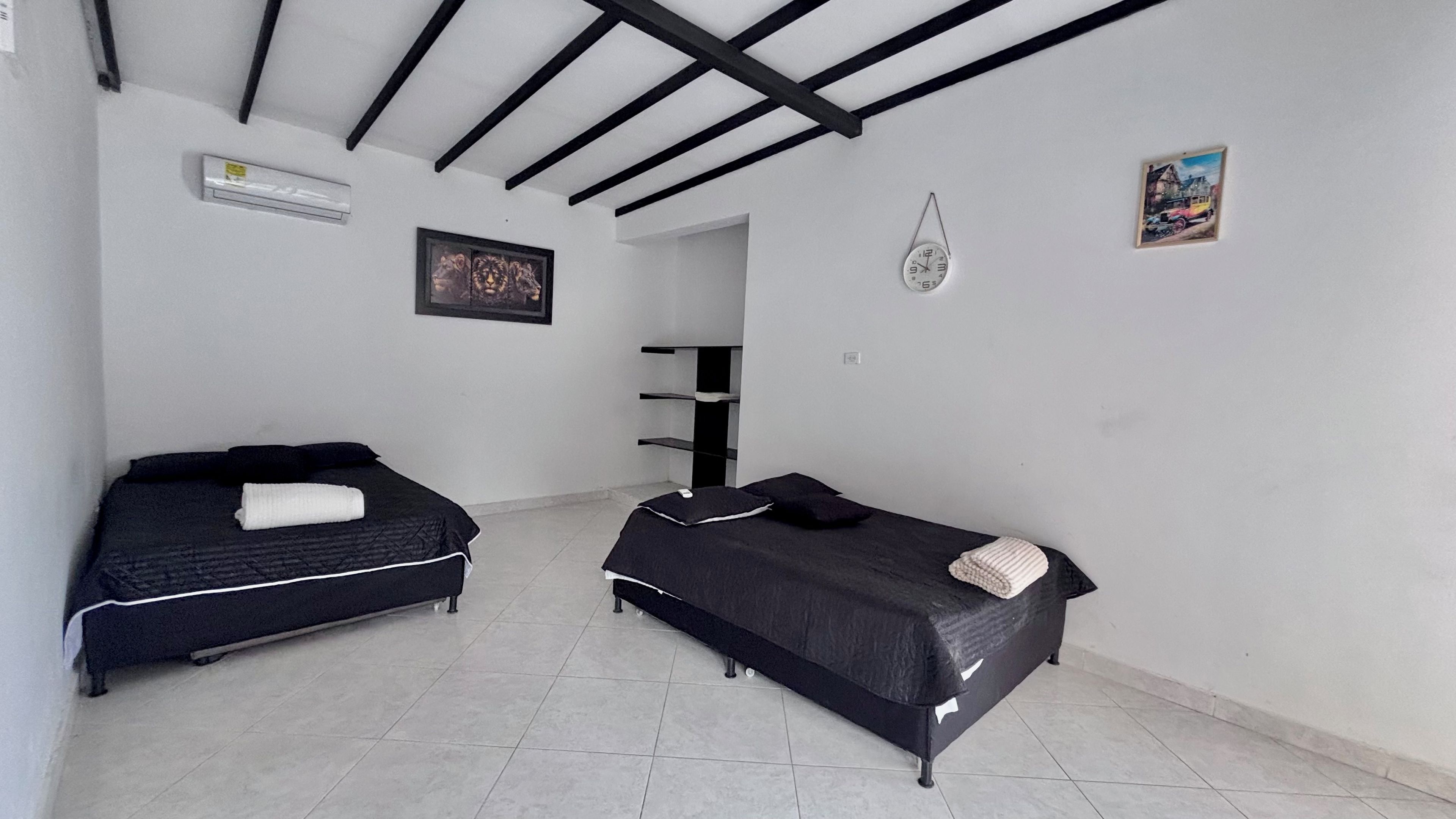A bedroom with two beds, a painting, a clock, and a small picture on the wall.