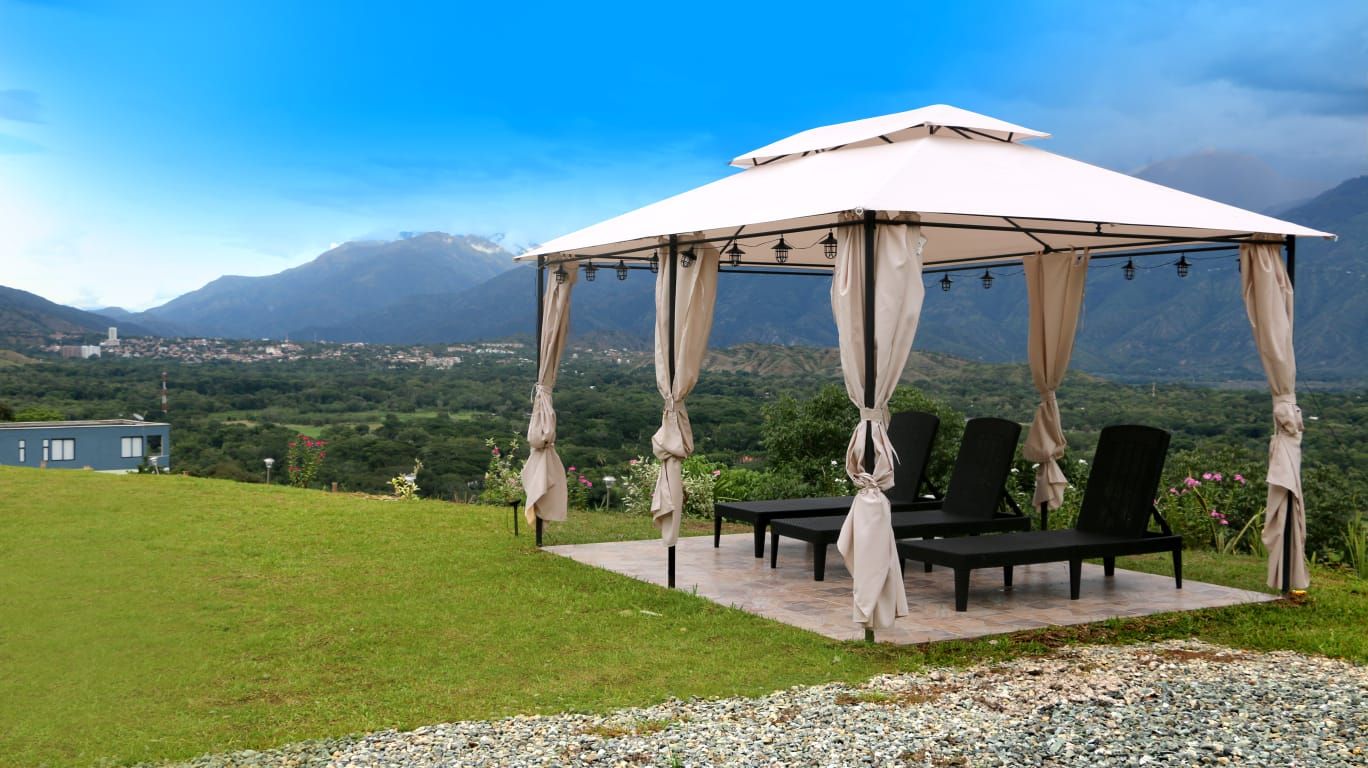 Un gazebo con tettoia bianca e sedie nere, posato su una piattaforma in pietra con vista su un paesaggio montuoso.