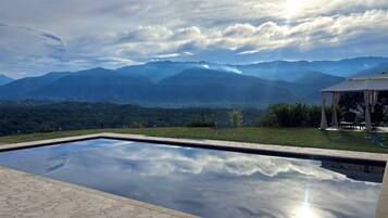 A swimming pool with a view of mountains and a gazebo with chairs.