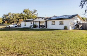 A single-story white house with a covered porch, a car parked in the driveway, and a grassy yard. - Golden Key Vacation Home Pool/Game (Brandon)