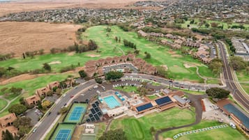 An aerial view of a golf course with a swimming pool, tennis courts, and a parking area.