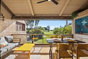 Un espace extérieur abrité, équipé d’une table et de chaises, d’un canapé et offrant une vue sur un terrain de golf.