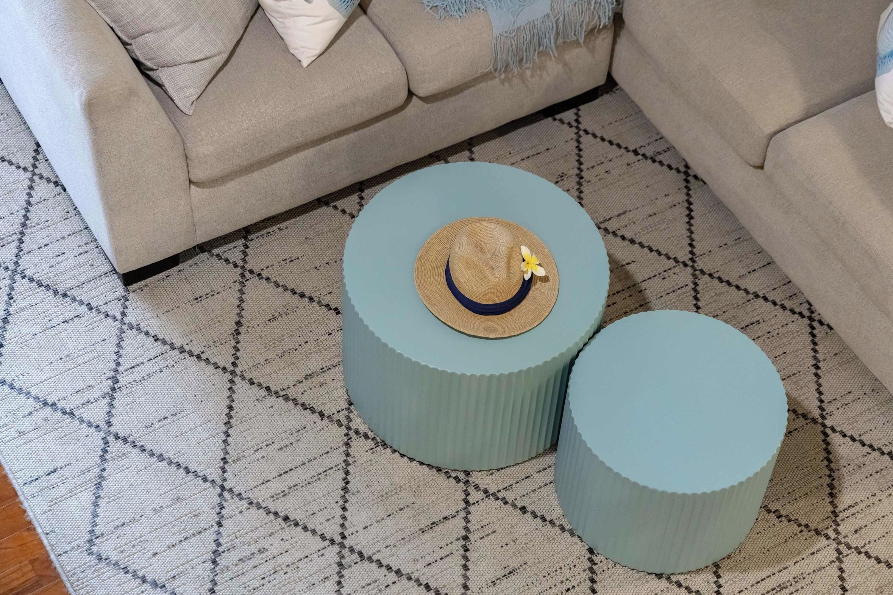 Une pièce avec un tapis à motifs, deux petites tables d’appoint rondes dont le plateau est en matière tressée, et un canapé beige.