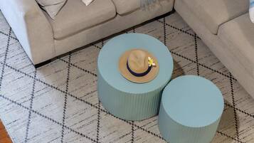 Une pièce avec un tapis à motifs, deux petites tables d’appoint rondes dont le plateau est en matière tressée, et un canapé beige.