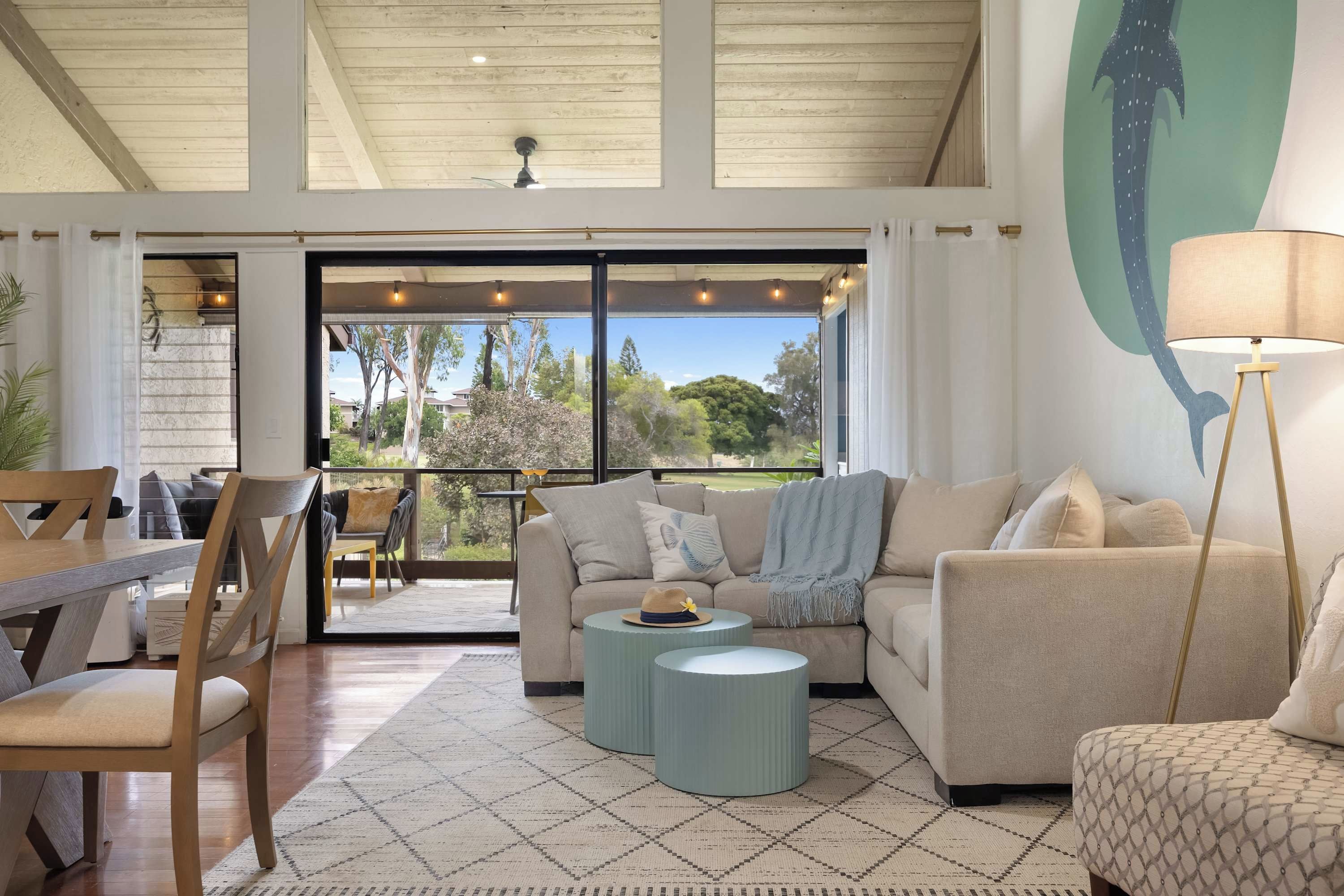 Un vaste espace de vie avec une grande porte-fenêtre coulissante donnant sur un patio extérieur, un coin salon comprenant un canapé et des fauteuils, et une lampe décorative.