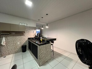A modern kitchen with a central island, pendant lighting, and a tiled floor. - Cozy, furnished apartment for rent in Porto Seguro. (Porto Seguro)