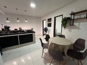 A modern kitchen with a dining area, featuring a central island, pendant lights, and a fan. - Cozy, furnished apartment for rent in Porto Seguro. (Porto Seguro)
