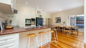 A modern kitchen with white cabinetry, granite countertops, and a dining area with wooden chairs and stools. - Cappa House, Kew by Property Mums (Kew)